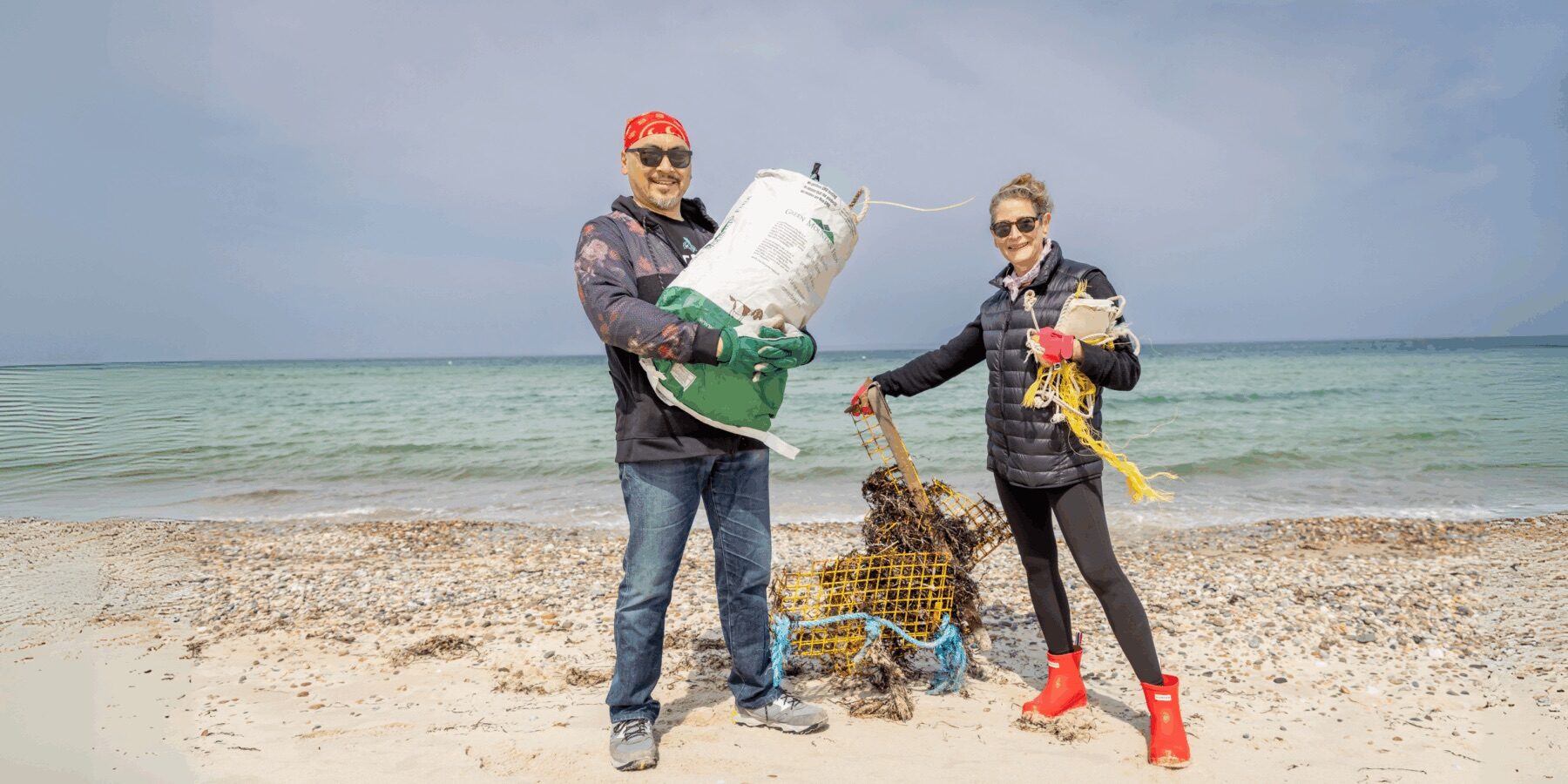 Two Vineyard Conservation Society volunteers standing on the beach collecting marine debris during a cleanup event.