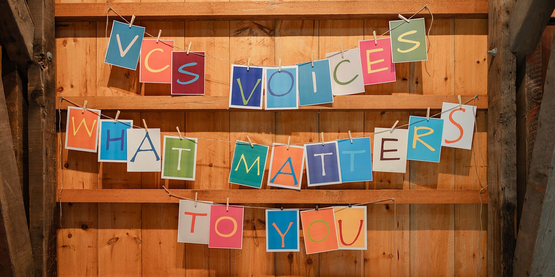 Colorful hanging sign reading “VCS voices what matters to you” against wooden wall