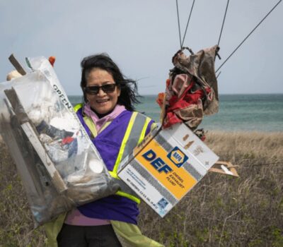 Beach Clean up volunteer holding up trash on shoreline