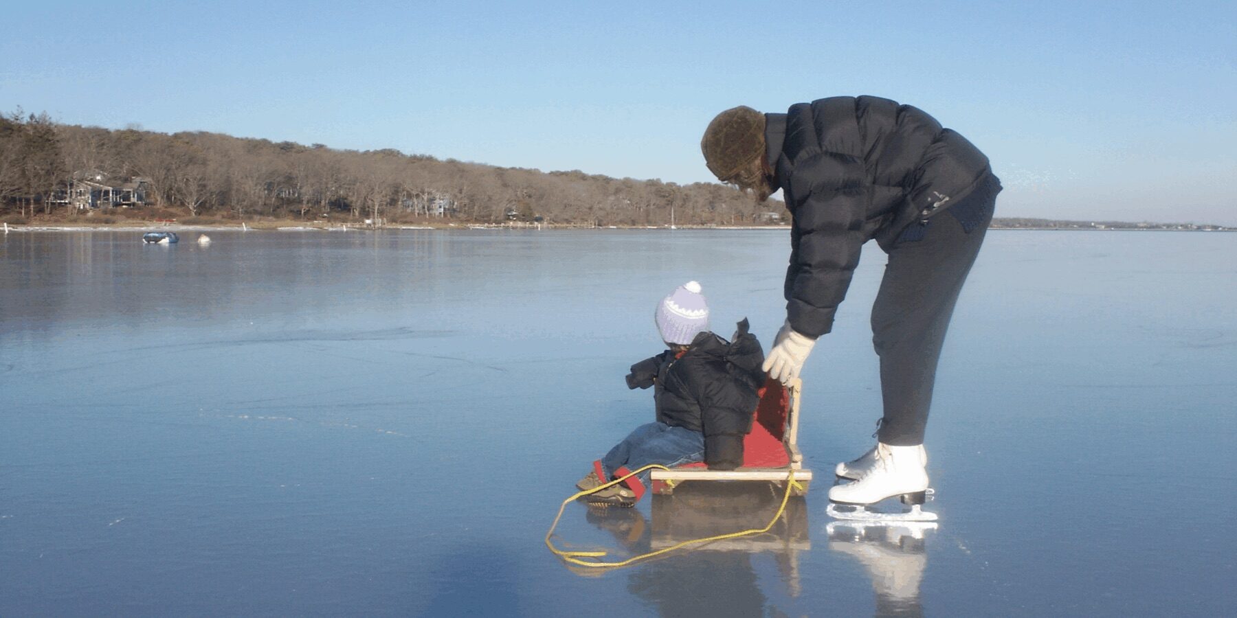 Adult pushing small child on sled in winter on Martha’s Vineyard frozen pond